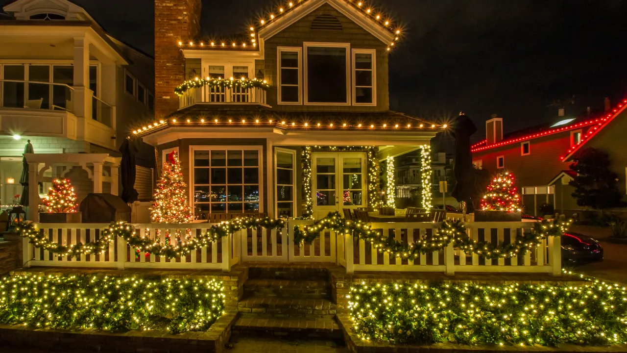 A house at night with warm white Christmas lights outlining its roofline, porch, railings and the shrubs in the front yard.