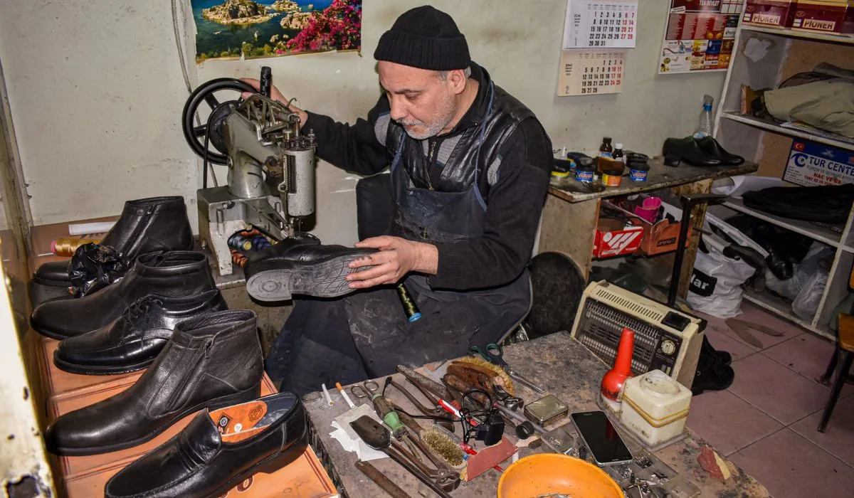 A cobbler repairing a shoe at a finishing machine surrounded by finished pairs